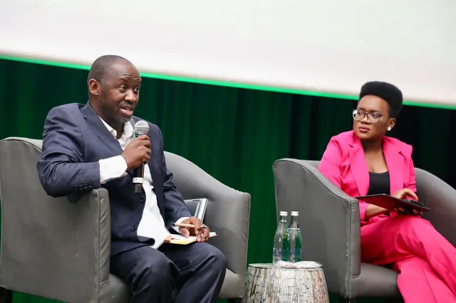 A panel speaker addressing the audience with a microphone alongside a fellow panellist