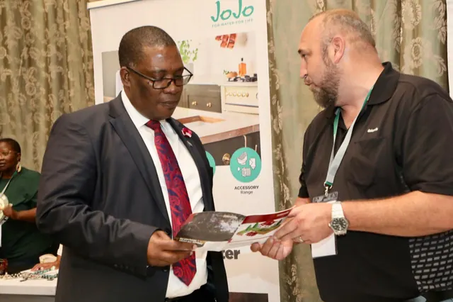 An exhibitor sharing a water infrastructure brochure with a visitor at the JoJo stand