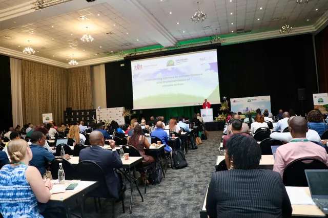 A speaker addressing delegates seated at tables in the main conference hall